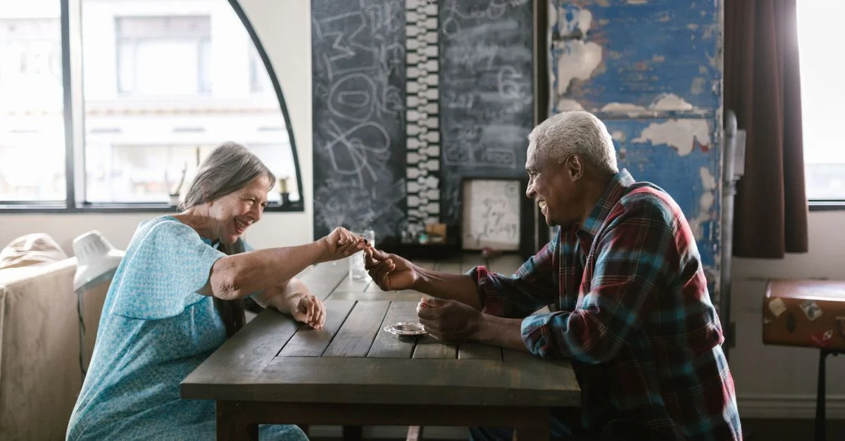Couple âgé riant et jouant à un jeu à une table à l'intérieur, profitant de la compagnie de l'autre.