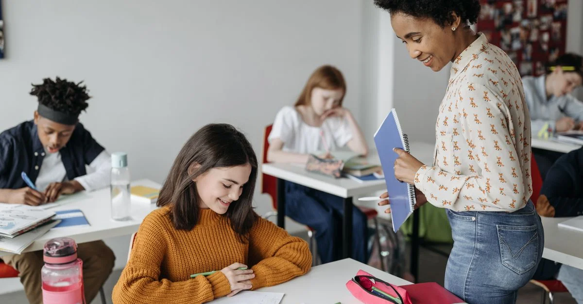 Enseignante aidant des élèves dans une salle de classe, favorisant un environnement d'apprentissage.
