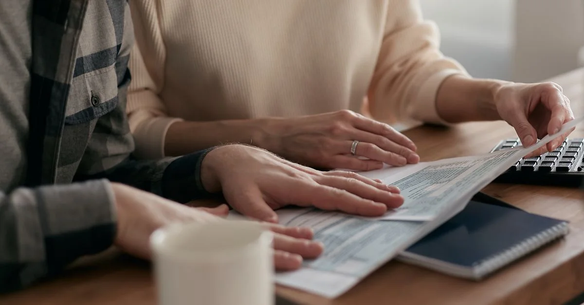 Un homme et une femme examinant des documents financiers sur une table en bois avec un clavier et une tasse de café.