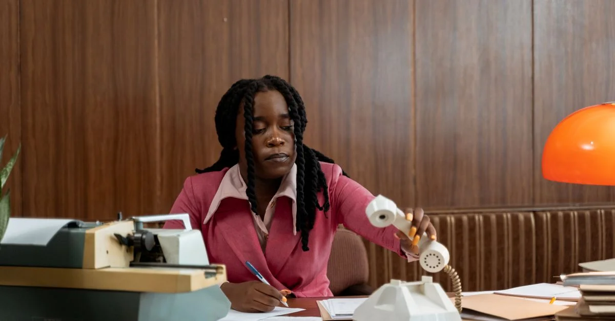 Une femme adulte dans un bureau vintage, utilisant un téléphone à cadran.