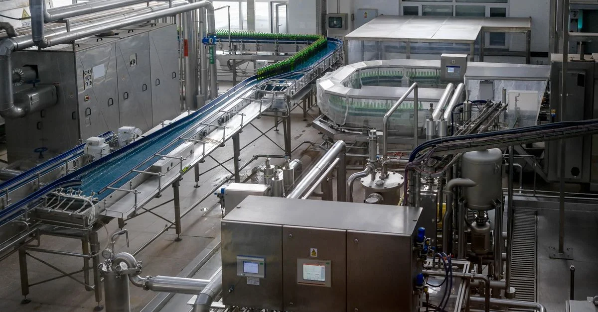Vue intérieure d'une usine automatisée d'embouteillage de boissons, avec machines et convoyeurs.