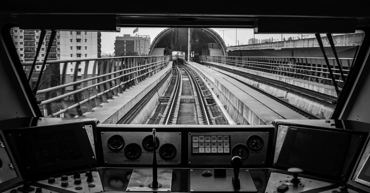 Photo monochrome depuis l'intérieur d'un poste de conduite de train montrant les rails et les manomètres.